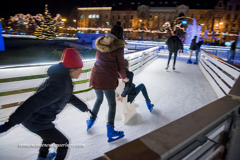 Plaza de Tomislavac o Plaza del Rey Tomislav. Foto en un pasillo con los lateras/protectores de madera se ve a personas patinando. Una madre esta empujando una silla de plástico donde esta sentado un niño