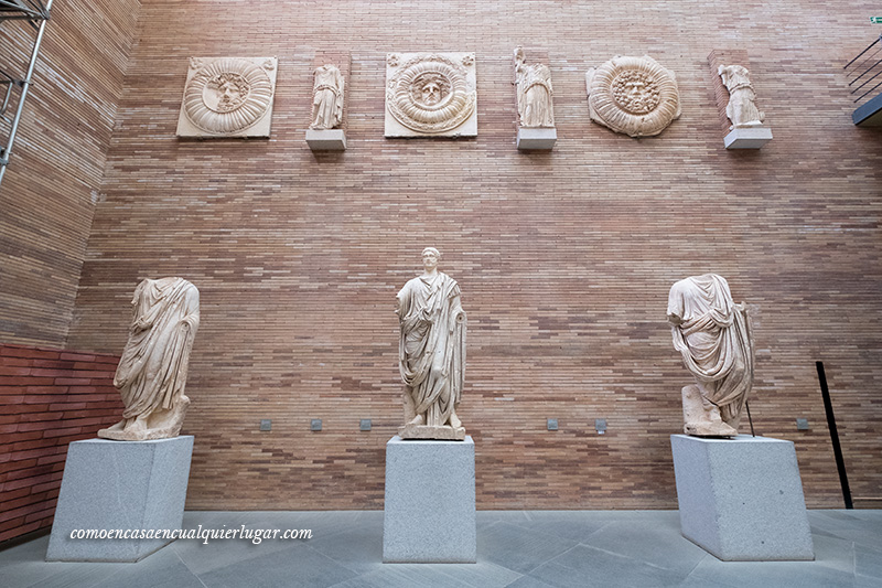 foto exposición restos romanos. Tres esculturas de personas, en los laterales sin cabezas y la del centro sin brazos, en la parte superior, esculturas más pequeñas.